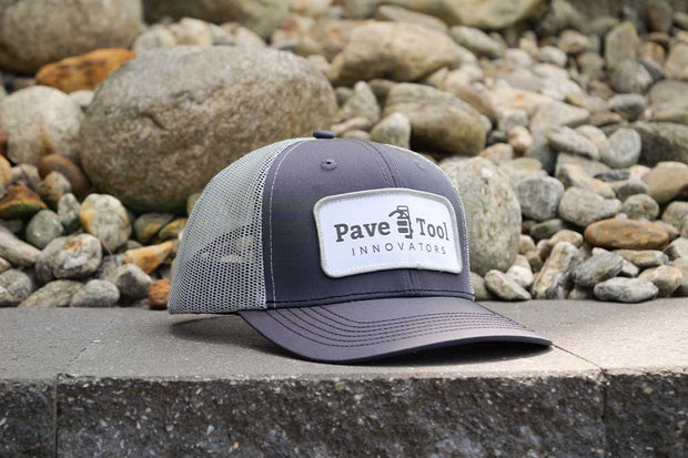 Navy blue cap with a white logo on a stone surface with pebbles in the background