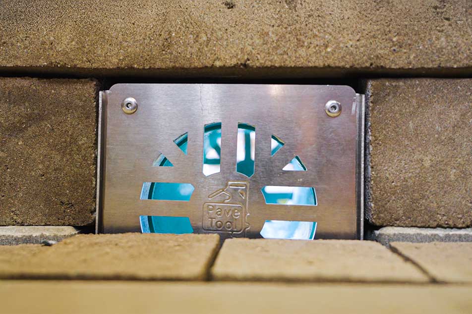 Metal drain cover embedded in a concrete wall with visible brand logo.