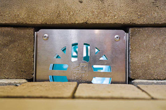 Metal drain cover embedded in a concrete wall with visible brand logo.