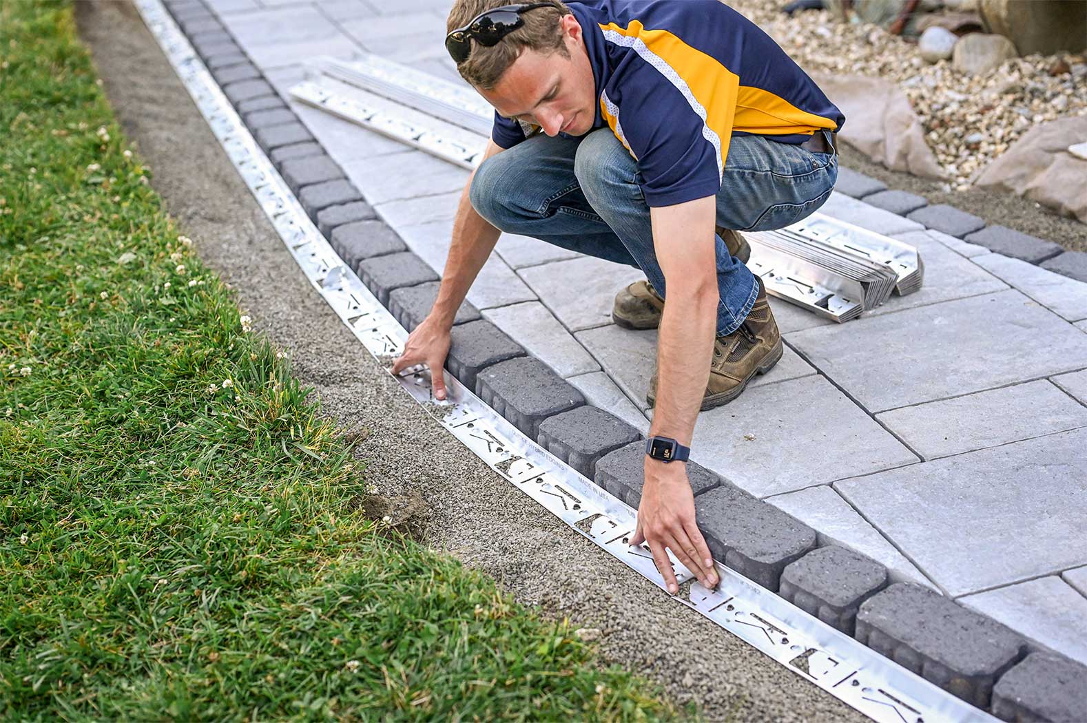 A person installing a gray, metal edging system for a garden or landscaping area.